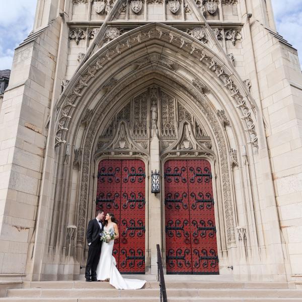 Bride and Groom standing outside of Heinz Chapel with red doors in background